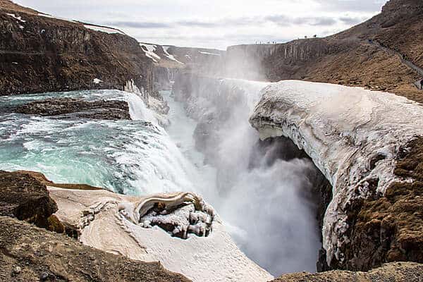 Cascading water falls between rock walls at the Gullfoss waterfall in Iceland.