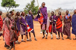 Travel Destination Kenya: Members of the Masai tribe, dressed in tunics in varying shades and patterns of purple and red, perform a dance. Once man can be seen jumping high in the air.