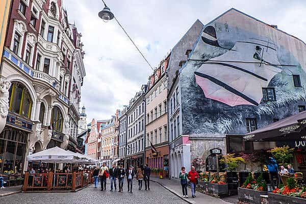 People walking in a street in Riga Old Town, lined with art nouveau and pastel painted, street art covered buildings.