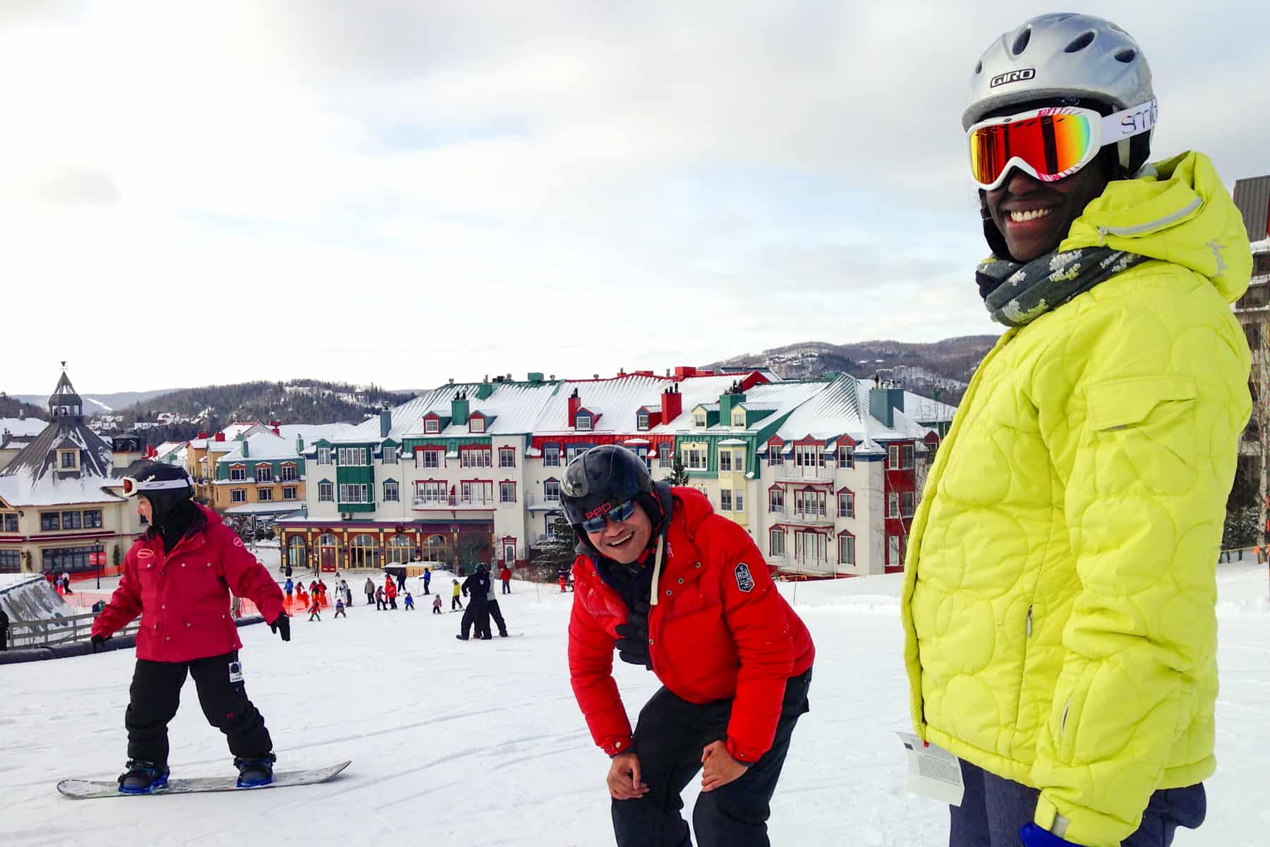 People in red and yellow jackets learning to snowboard on a beginner slope in Mont Tremblant village in winter. 