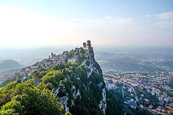 San Marino's fortress towers on the tip of hill and old town buildings cascading down it behind it. 