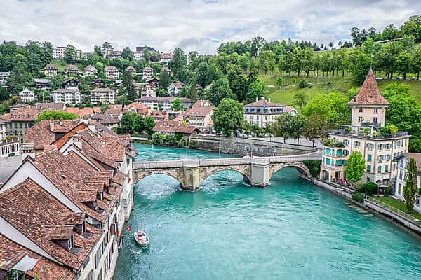 The red-roofed buildings of Bern Old town and the aqua Aare River flowing through a triple arched bridge. 
