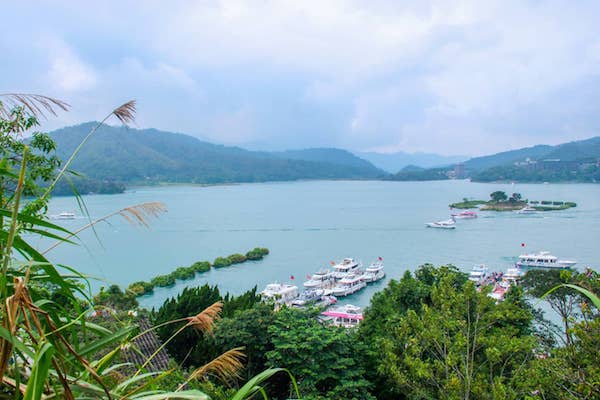 View through foliage of moored white boats on the wide turquoise waters of Sun Moon Lake in Taiwan. 