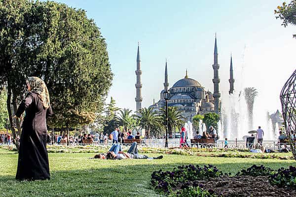 People lounging on the green lawn in front of the four minaret Sultanahmet Blue Mosque in Istanbul. 