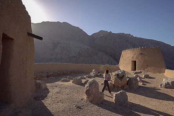 A woman walking within the turrets and wall fortifications in the mountain backed desert landscape of Ras Al Khaimah.