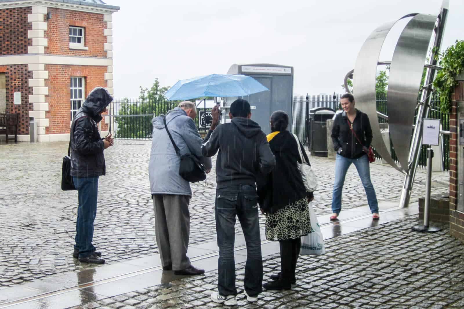 A group of five people standing next to Greenwich Prime Meridian Line in London on a visit