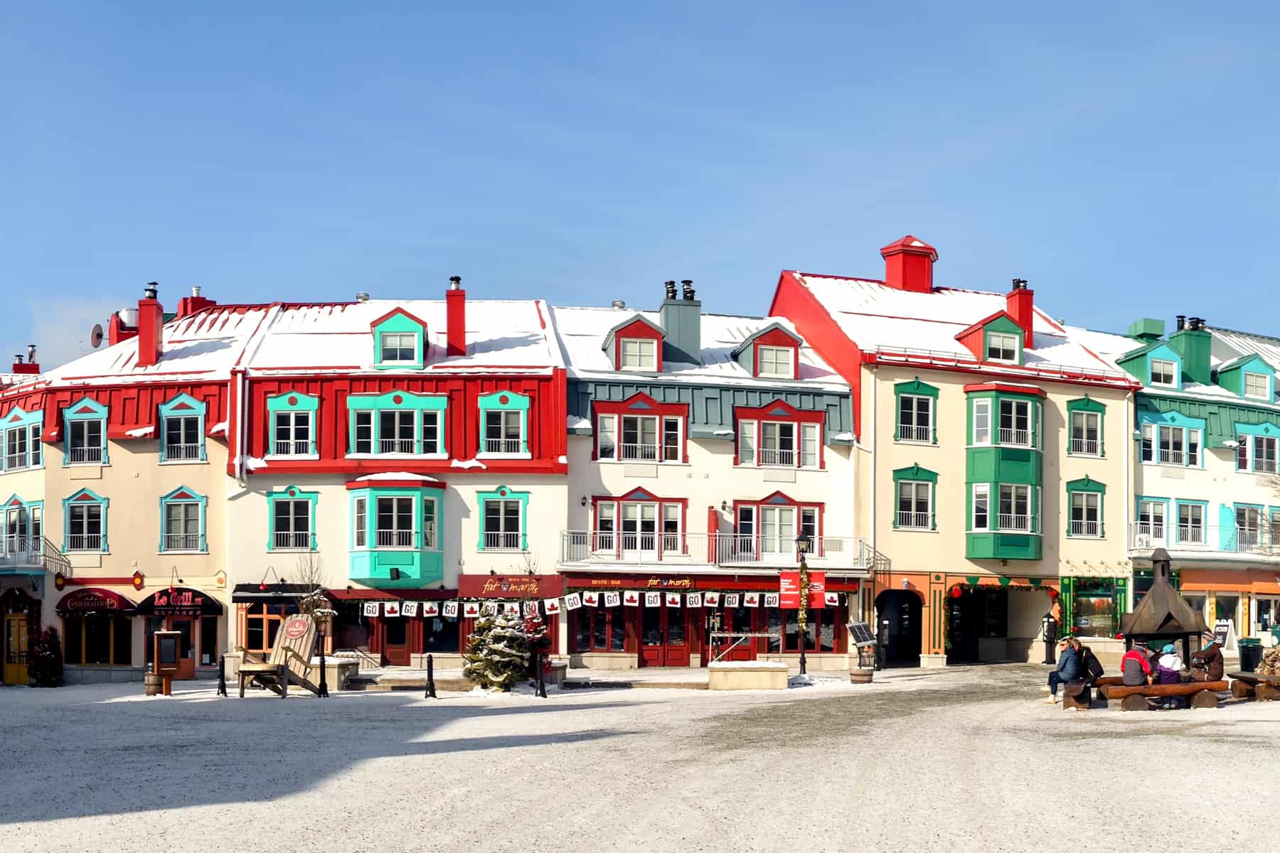 A row of buildings painted in red, mint green and yellow in Mont Tremblant's winter village.