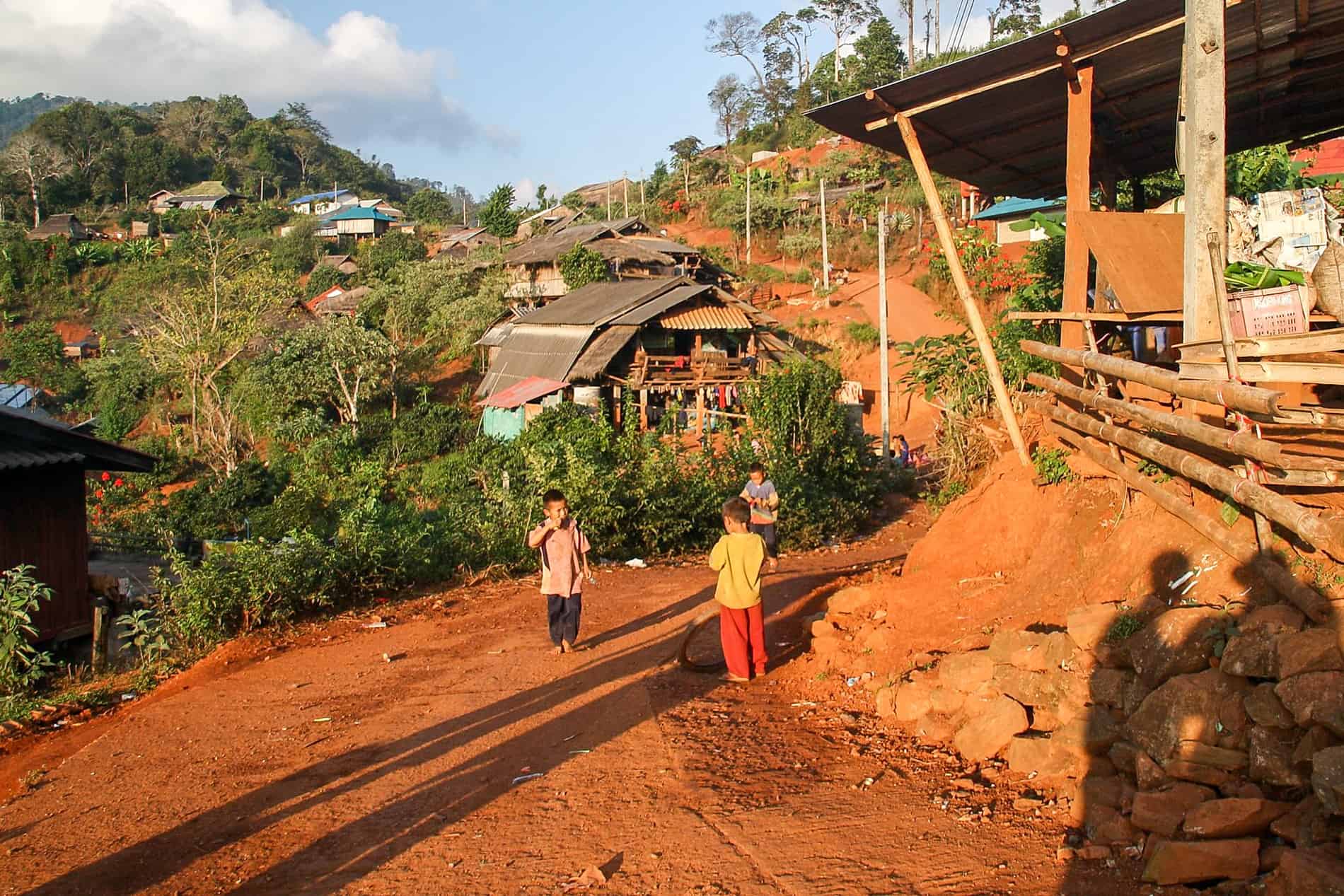 Three children play on the red dusty path of a hilltop village in Thailand. 