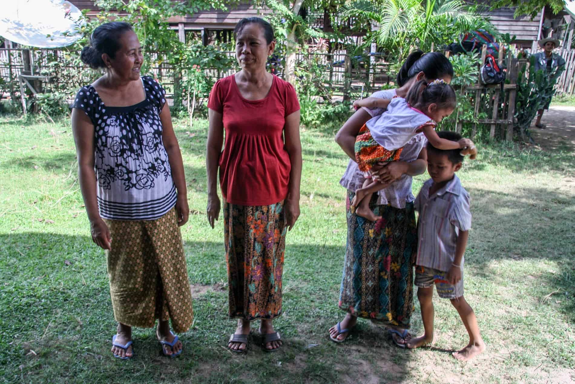 Three woman, one with two children, stand in the garden outside their home in Laos. 