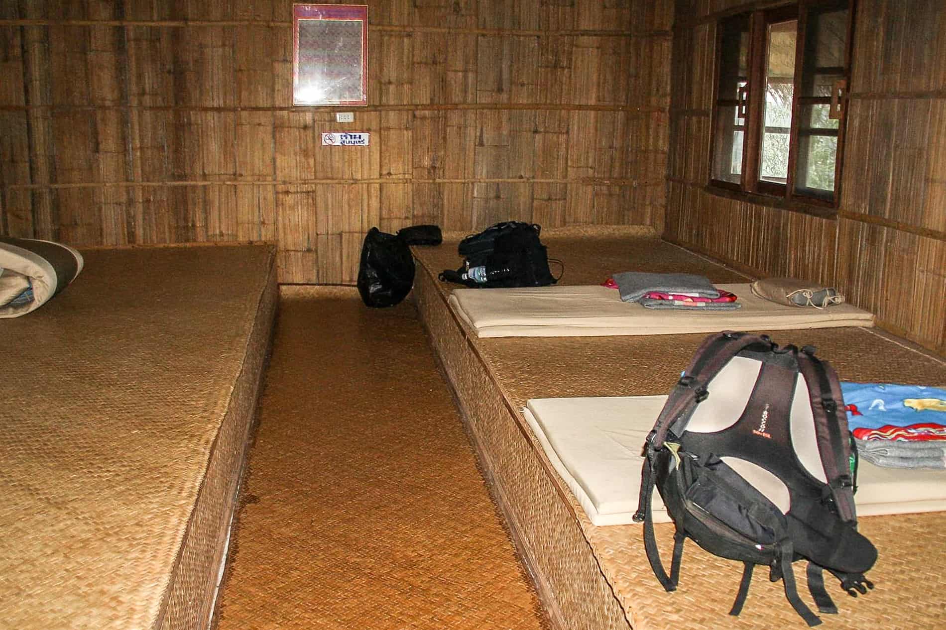 Sleeping mats and backpacks laid out in a bamboo room at a homestay in Asia. 