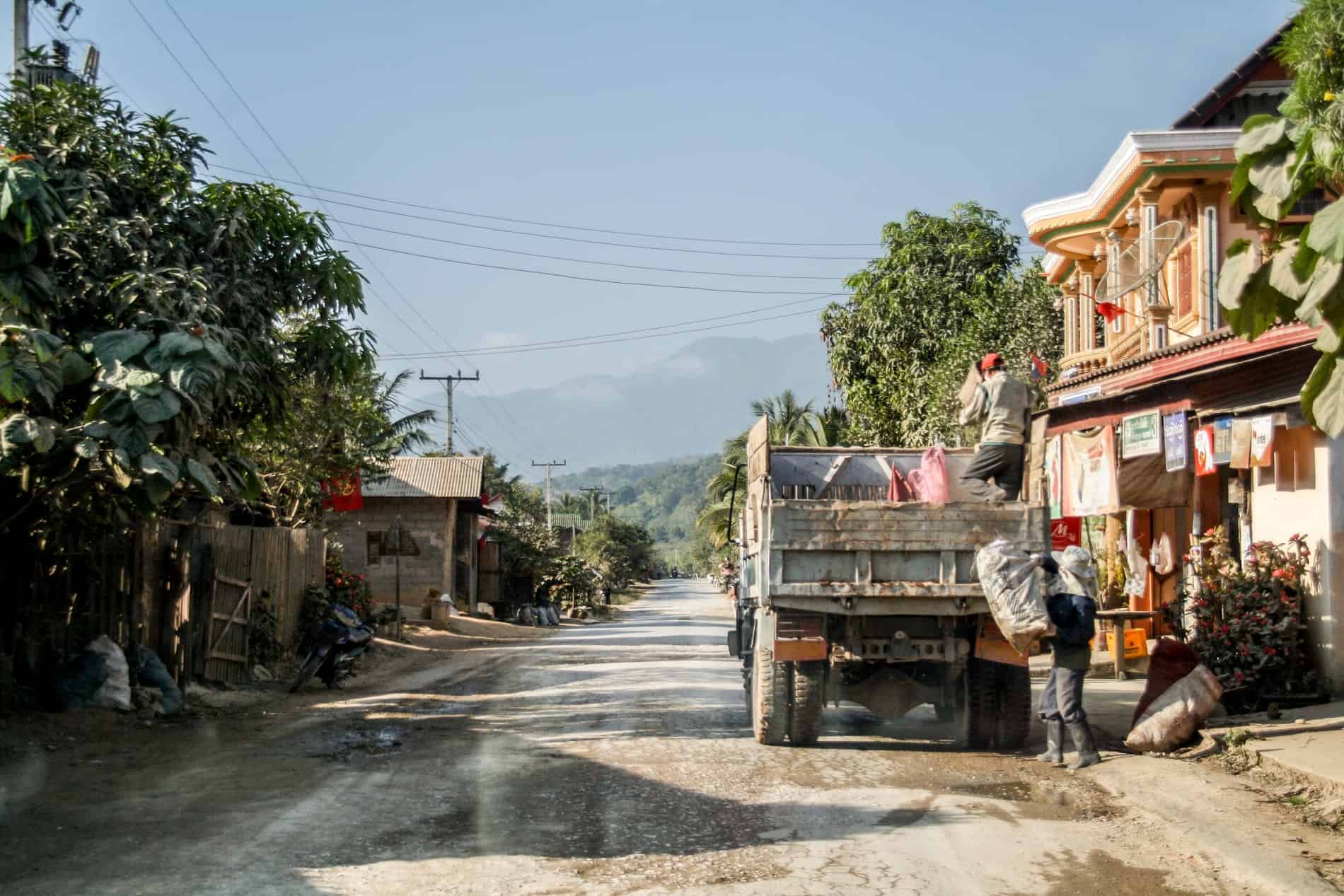 Two mean load heavy bags onto the back of a truck in a forest-set village in Laos. 