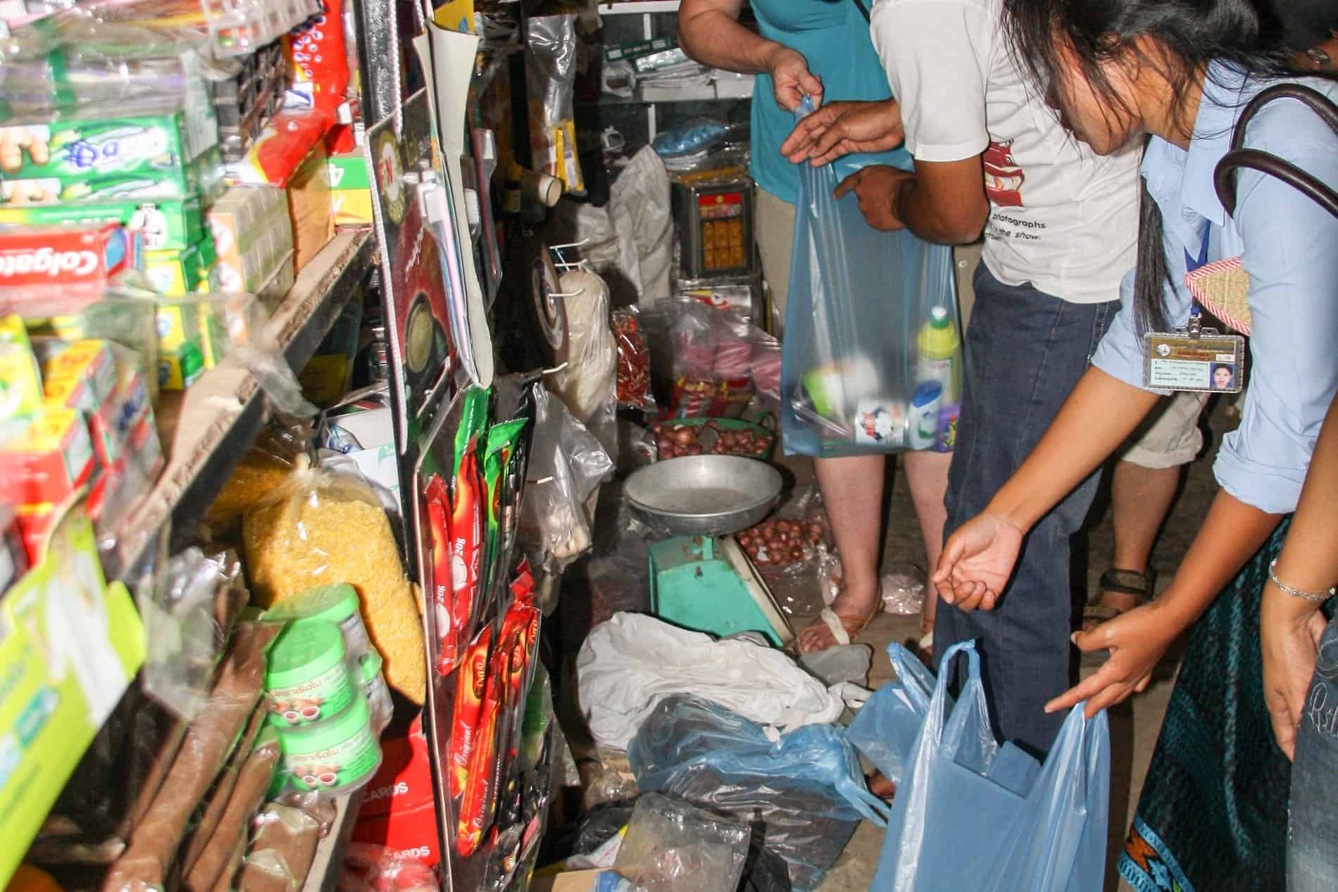 A woman holds open a blue plastic bag while shopping at a tiny convenience store in a village in Laos. 