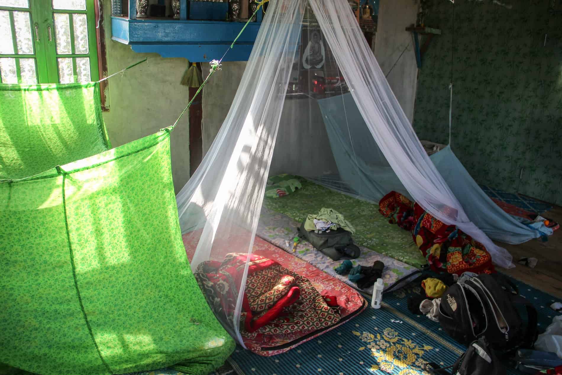 Two sleeping mats and piles of clothing under a white mosquito net is a communal homestay. 
