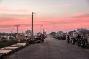 A long street lined with blankets, street food carts, motorbikes and makeshift tents under a dusky pink sky in Siem Reap, Cambodia