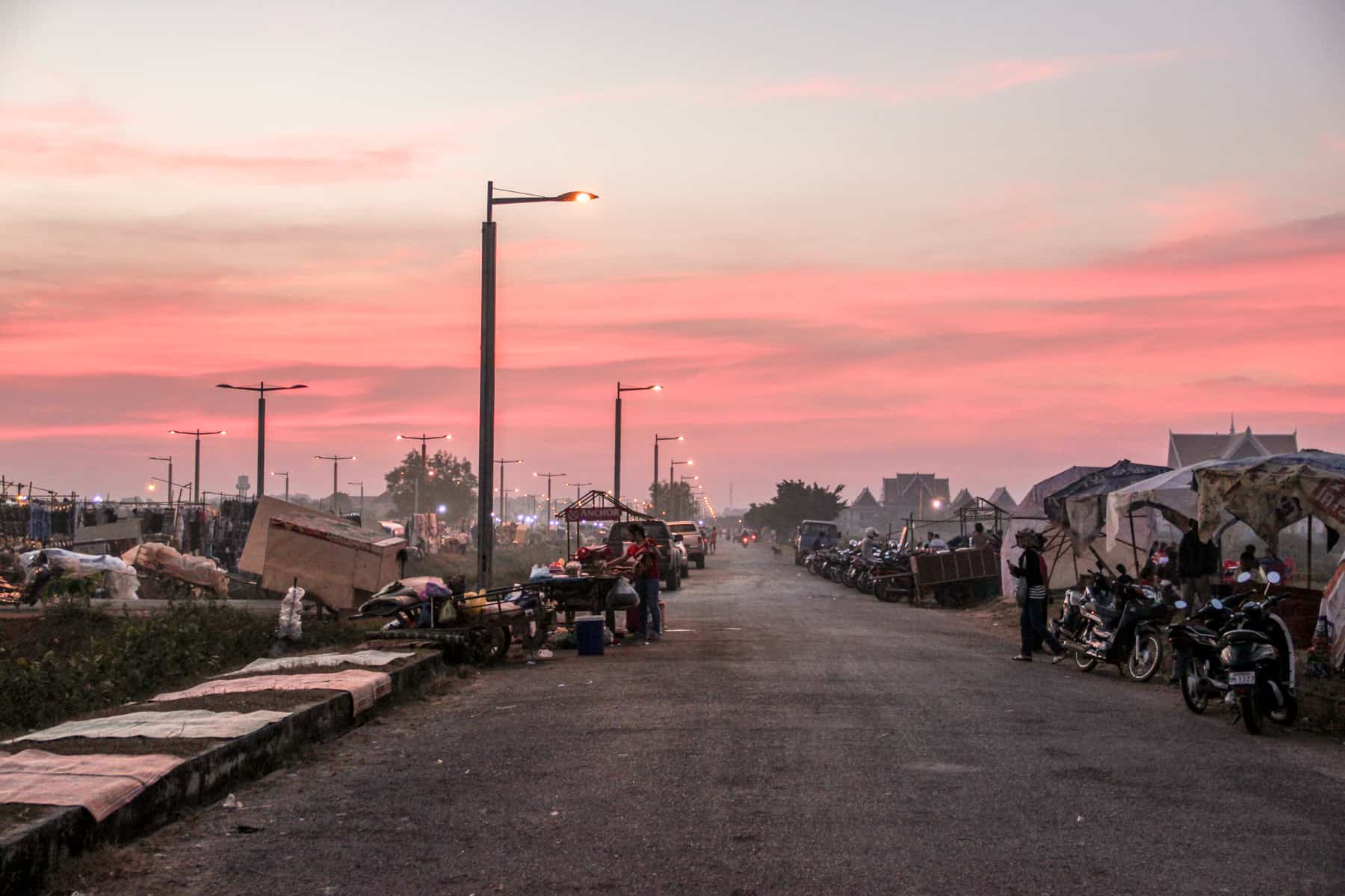 60 Road Siem Reap – A long street lined with blankets, street food carts, motorbikes and makeshift tents under a dusky pink sky in Siem Reap, Cambodia