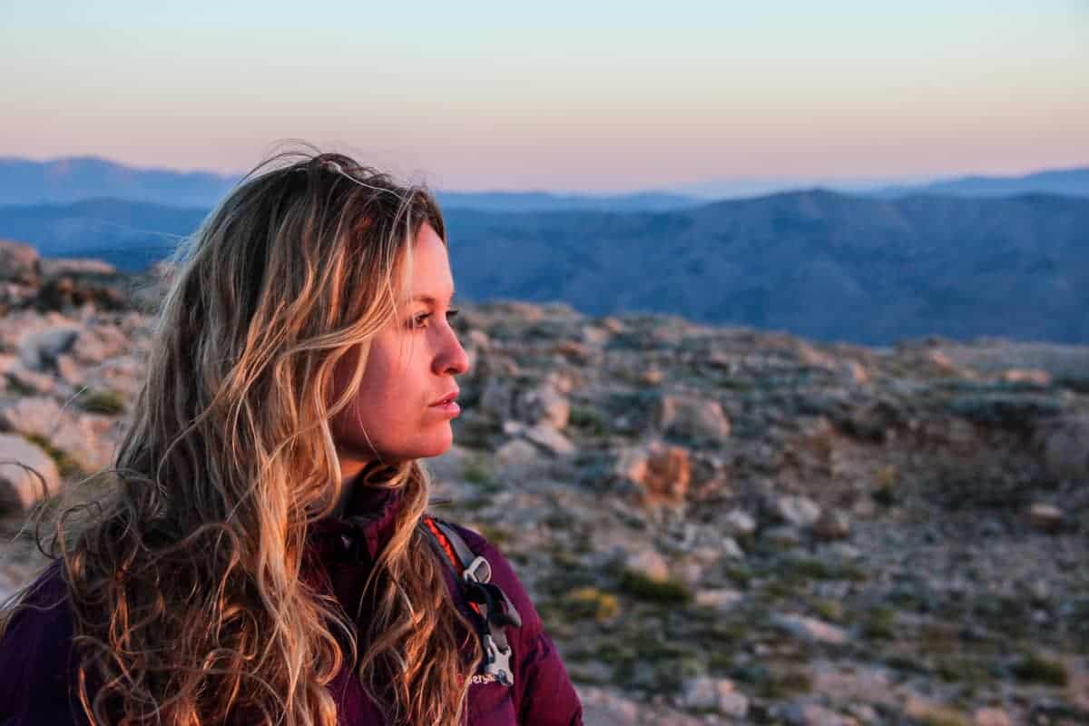 Becki Enright from Borders of Adventure on top of a mountain looking towards the horizon. 