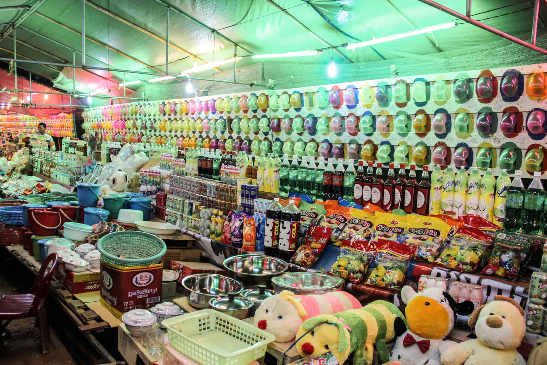 Sweets, fizzy drinks and soft toys line a fun fair games stall set within a green tent. 