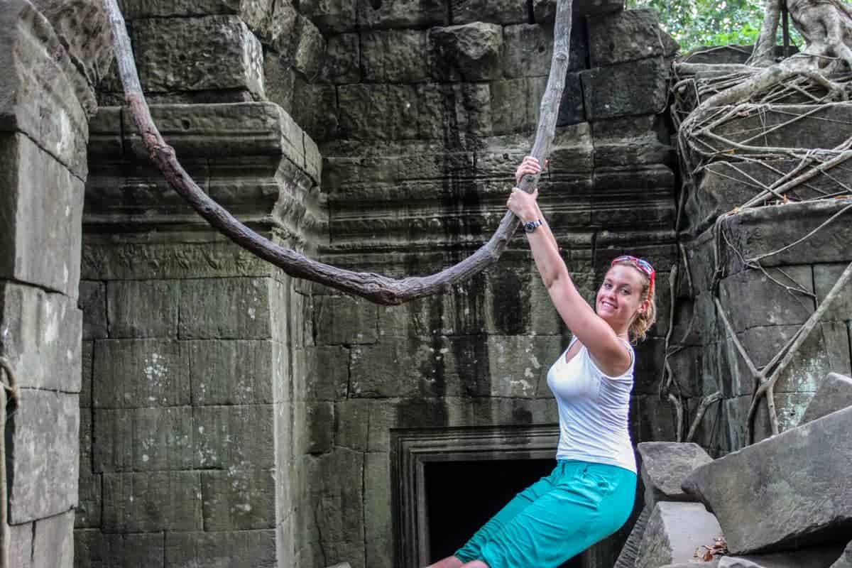 A woman swings on a large, thick, curved branch that hangs inside the Beng Mealea temple in Cambodia