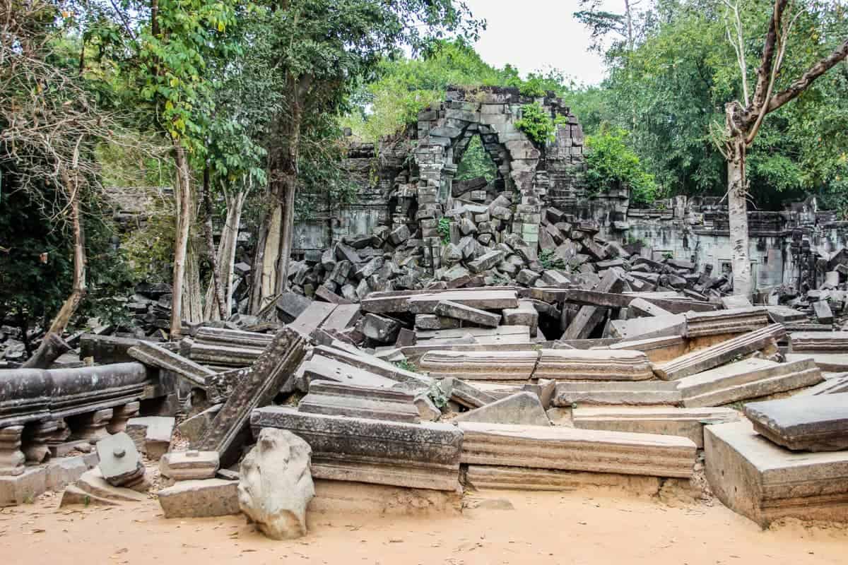 Long rectangular stones stacked in front of an old Angkor temple archway that makes Beng Mealea look like it was only just discovered