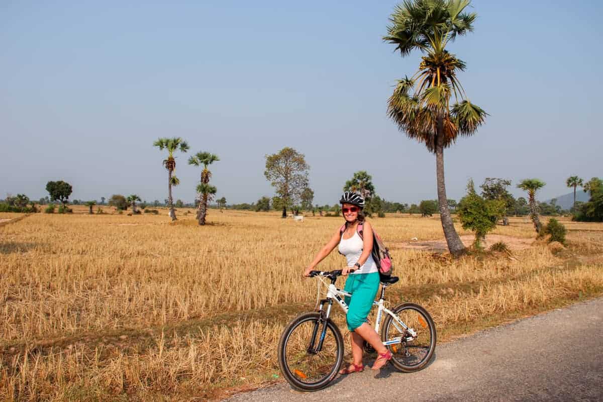 A woman on a bike next to a field of golden yellow flanked by tall trees