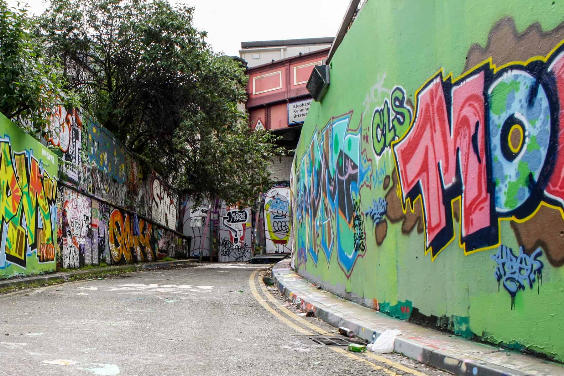 An alleyway with a dead end under an old railway bridge, whose walls are covered in Graffiti. 