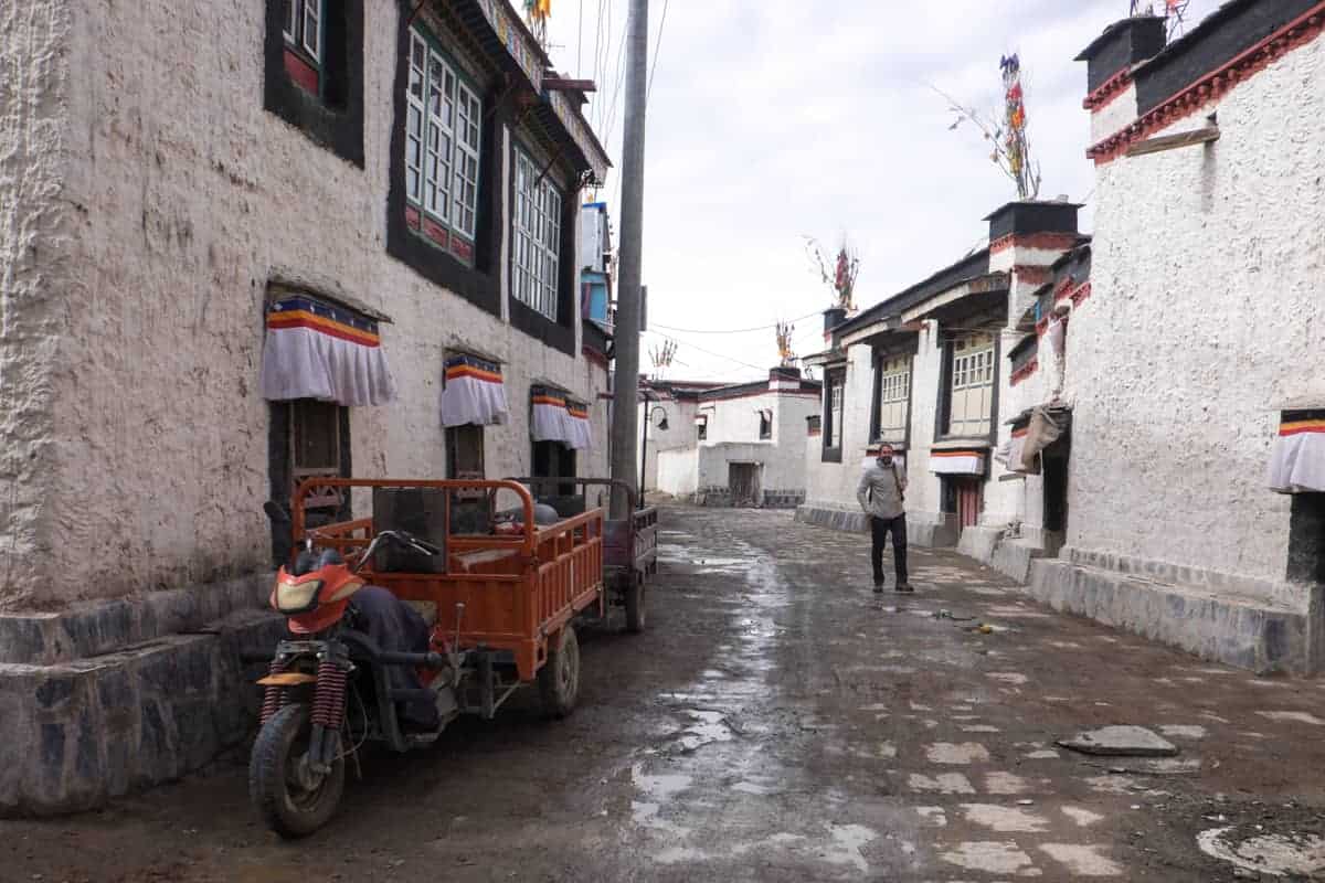 Turista masculino camina en el pueblo tranquilo y tradicional de Gyantse, lleno de casas tibetanas blancas con ventanas con adornos negros