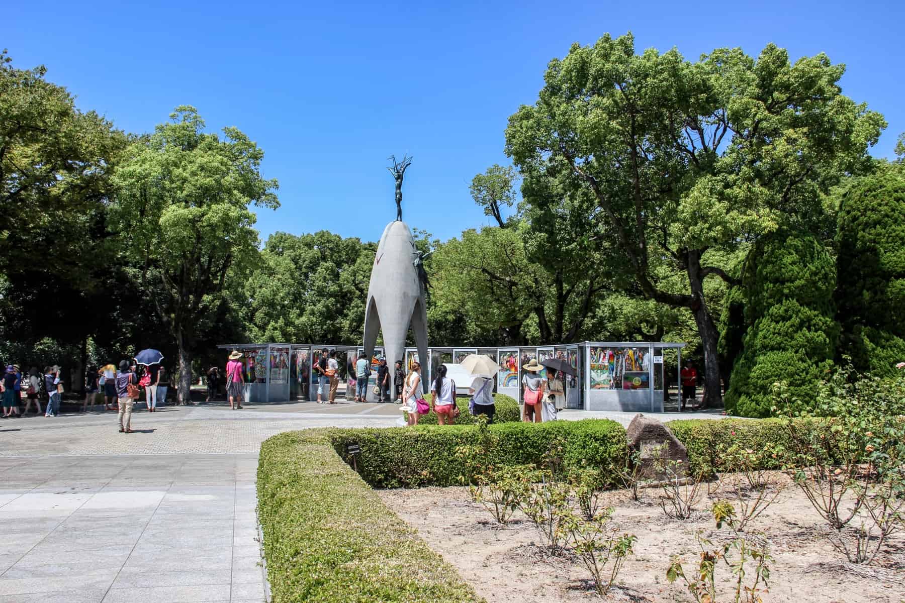 People gather around the bomb shaped, figure topped Children’s Peace Monument in the Hiroshima Peace Park Memorial. 