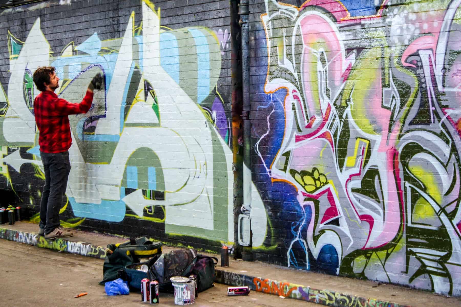 A man spray painting on a brick wall in the London graffiti tunnel. 