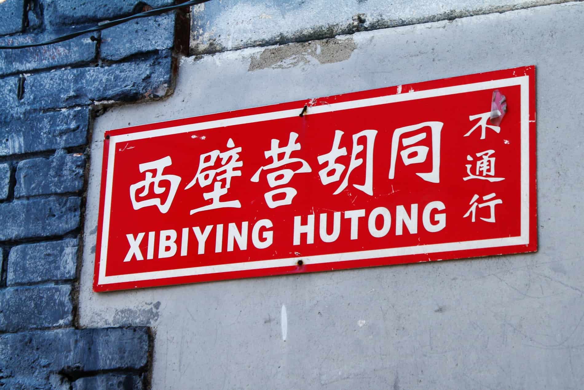 A red street sign with white writing for a Hutong in China