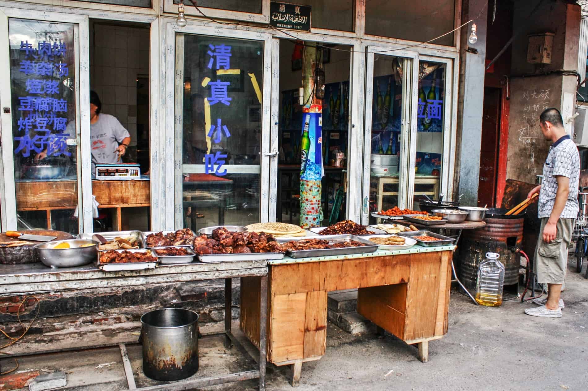 A man standing at a grill need to a long table of cooked meats. 