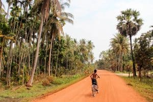 A young boy rides cycles on an orange dusty road in a village in Cambodia