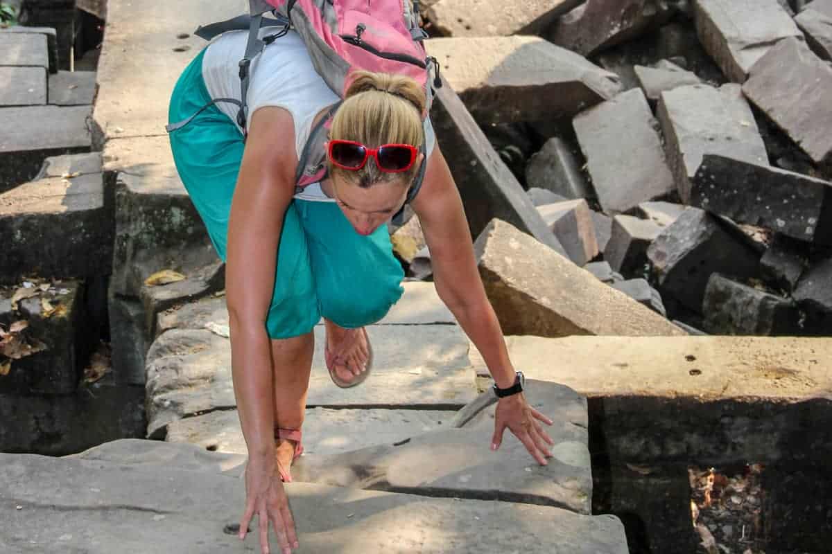 A woman uses her hands and feet in order to climb the fallen temple complex of Beng Mealea which is covered and damaged by nature