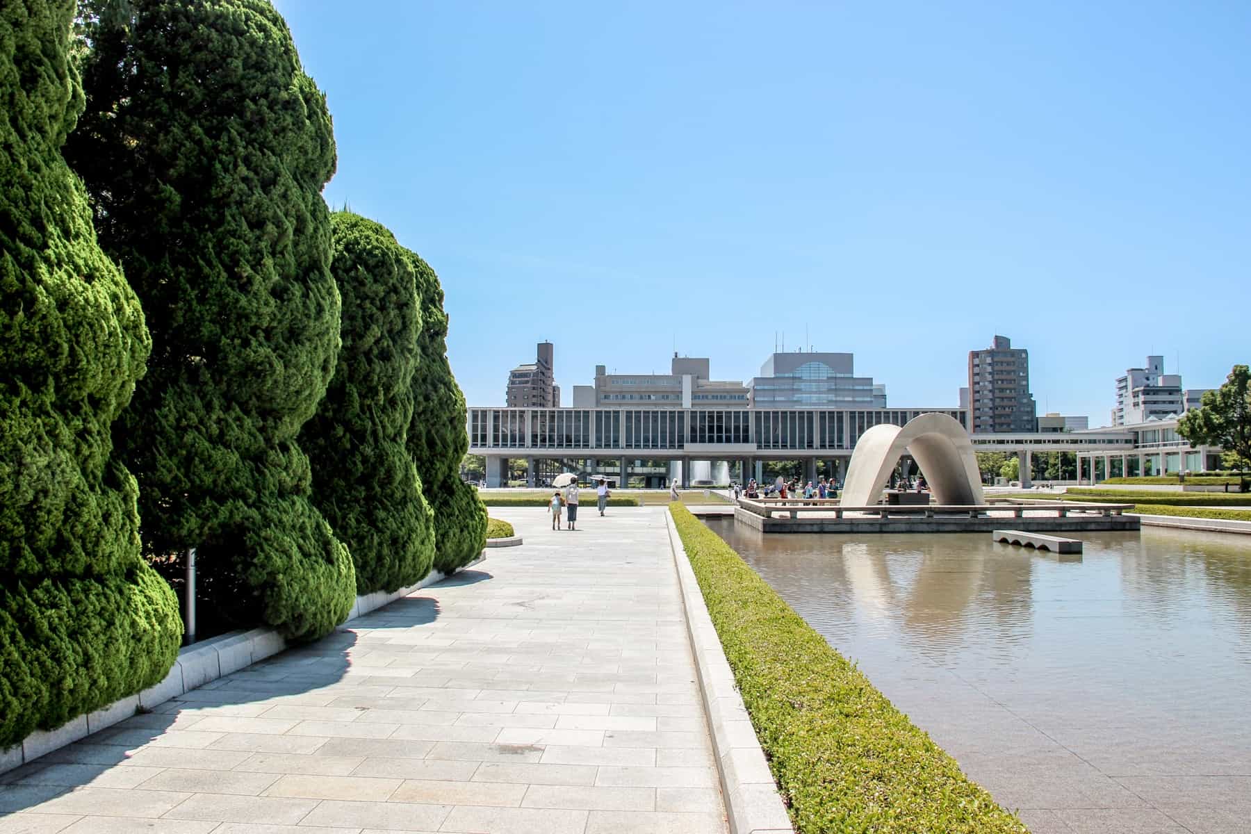 The long grey building of the Hiroshima Peace Memorial Museum at the end of the green and water-filled Peace Park. 