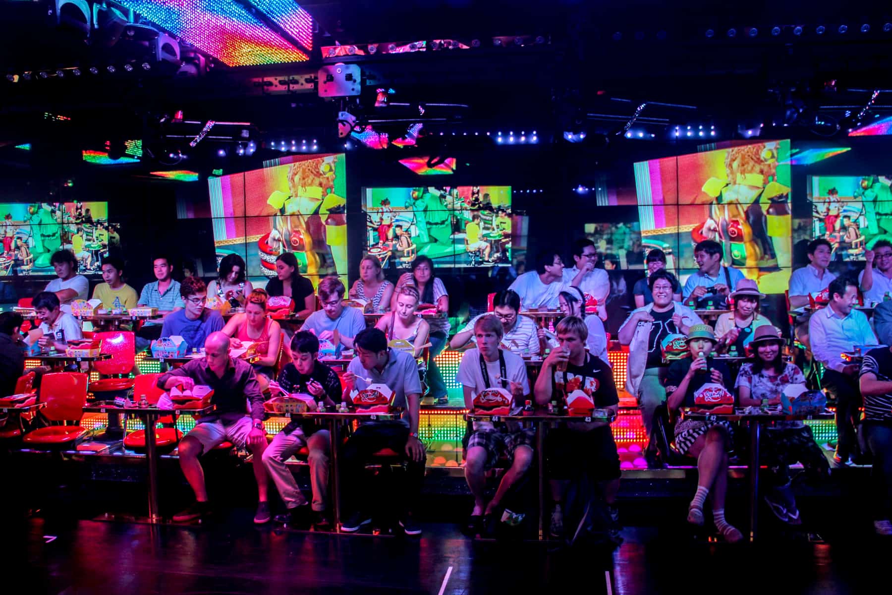 The audience at the Robot Restaurant show in Tokyo, eating from snack boxes to a backdrop of neon lights. 