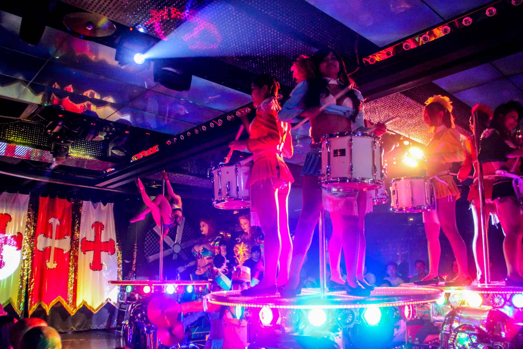 Women pole dancing and playing drums during a Tokyo Robot Restaurant show performance. 