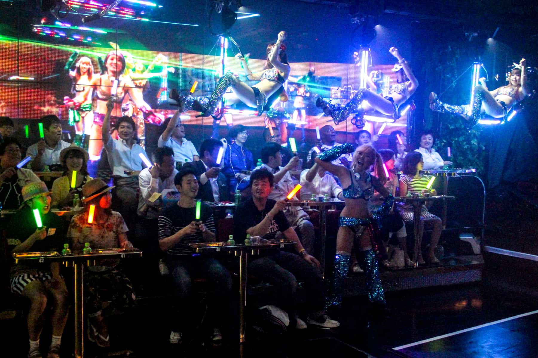Women ride above an audience waving glow sticks at the Robot Restaurant in Tokyo. 