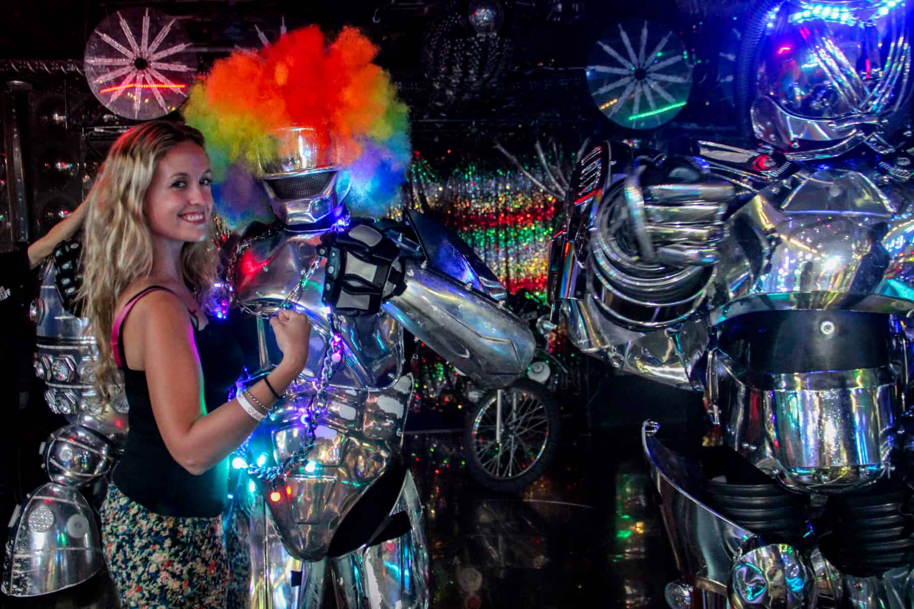 A woman standing with two giant robots (one with a multi coloured wig) at the Tokyo Robot Restaurant. 