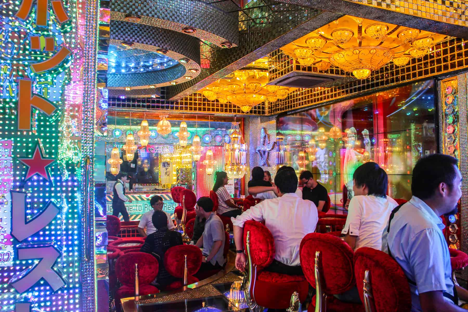People sit in red velvet chairs at the multicoloured and gold tile covered bar at the Robot Restaurant in Tokyo.