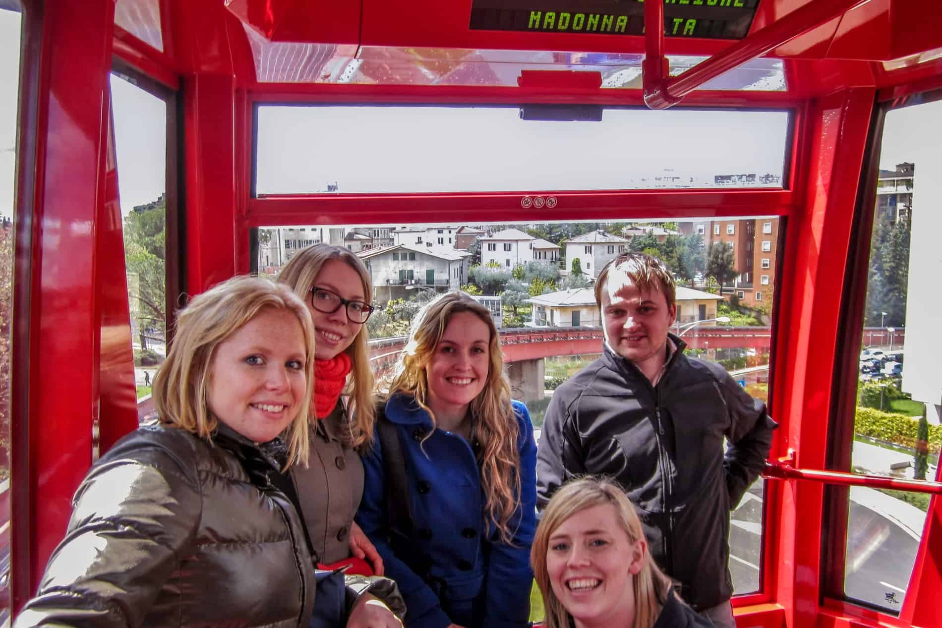 Five people crammed into the tiny red carriage of the Perugia Minimetro to a backdrop of the hillside city houses. 