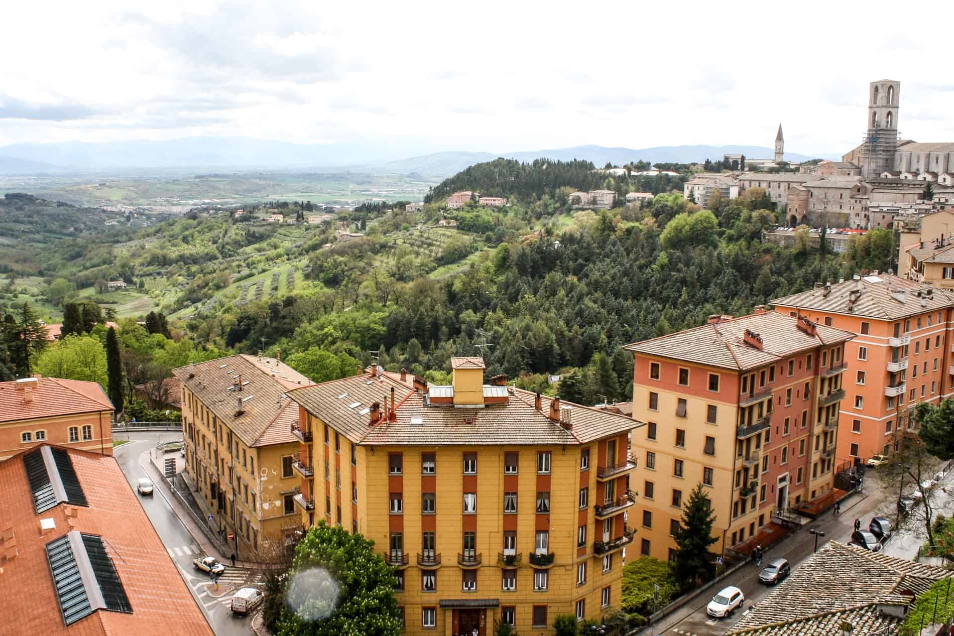 Elevated view of orange and yellow buildings in Perugia city overlooking the rolling hills of the Umbrian countryside. 