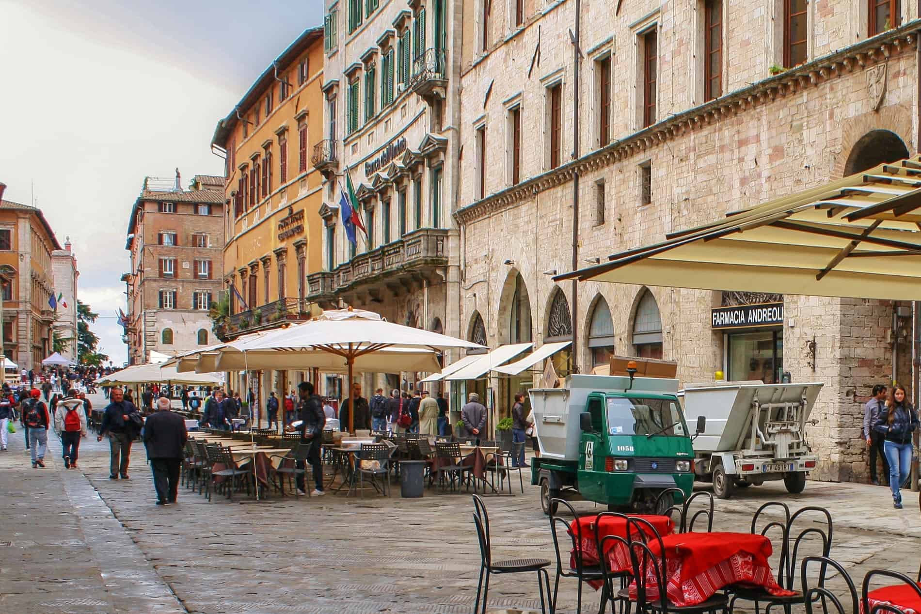 Orange and yellow hued and golden stone buildings on a busy pedestrian street in Perugia old town. 