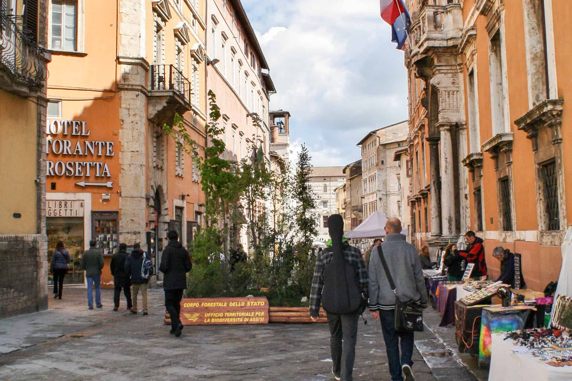 Street vendors and visitors in the old town of Perugia lined with orange buildings. 