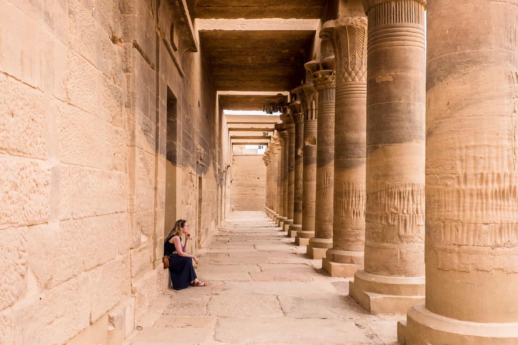 A woman sits within the corridor of columns at the Philae Temple in Aswan, Egypt