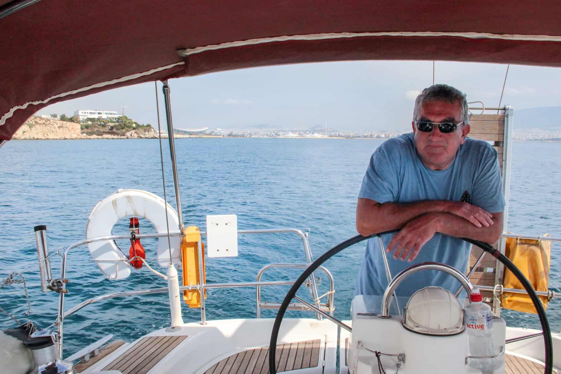 A skipper leans on the steering wheel of his yacht while out at sea on the Athenian Riviera. 