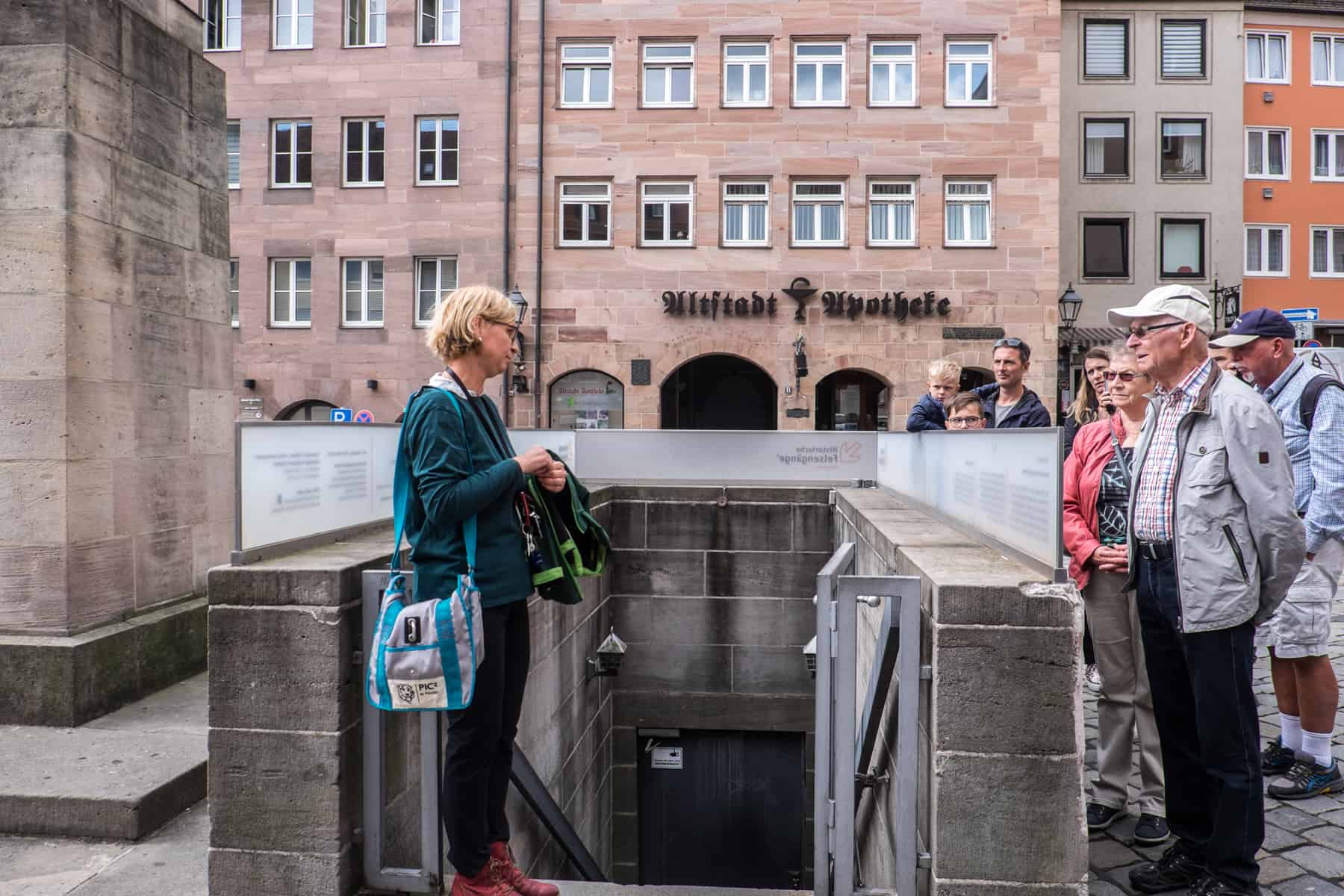 A woman with blonde hair stands at the entrance to an underground cellar in Nuremberg as a small group looks on - part of a daily rock cut beer cellar tour