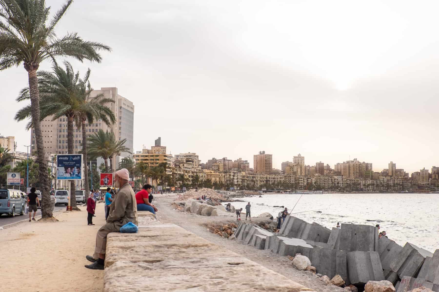 An old man sits on the stone wall that lines the pedestrian walkway and coastline of the northern city of Alexandria in Egypt