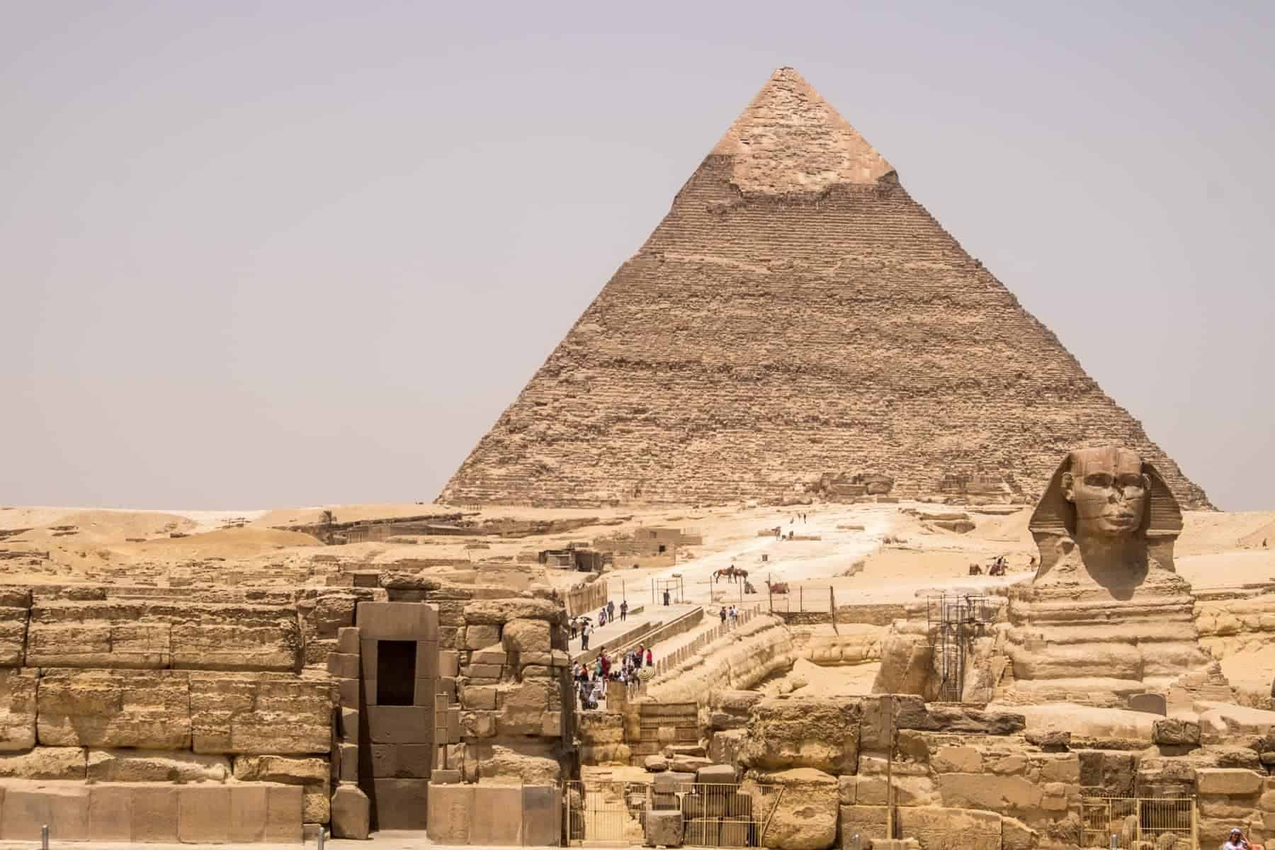 A great pyramid of Giza looms behind the sphinx in the dusty desert area of Giza in Egypt.