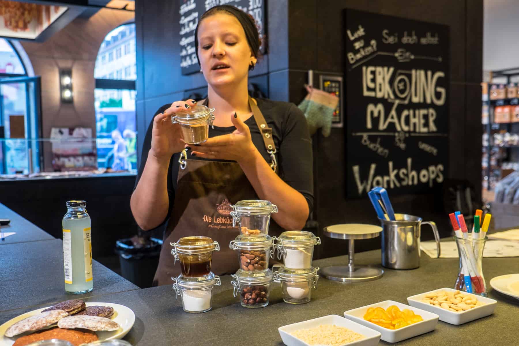 A woman at the Wicklein Lebkuchen in Nuremberg gives a baking glass and is explaining the different spices in each jar. The final result, baked gingerbread can be seen on the left