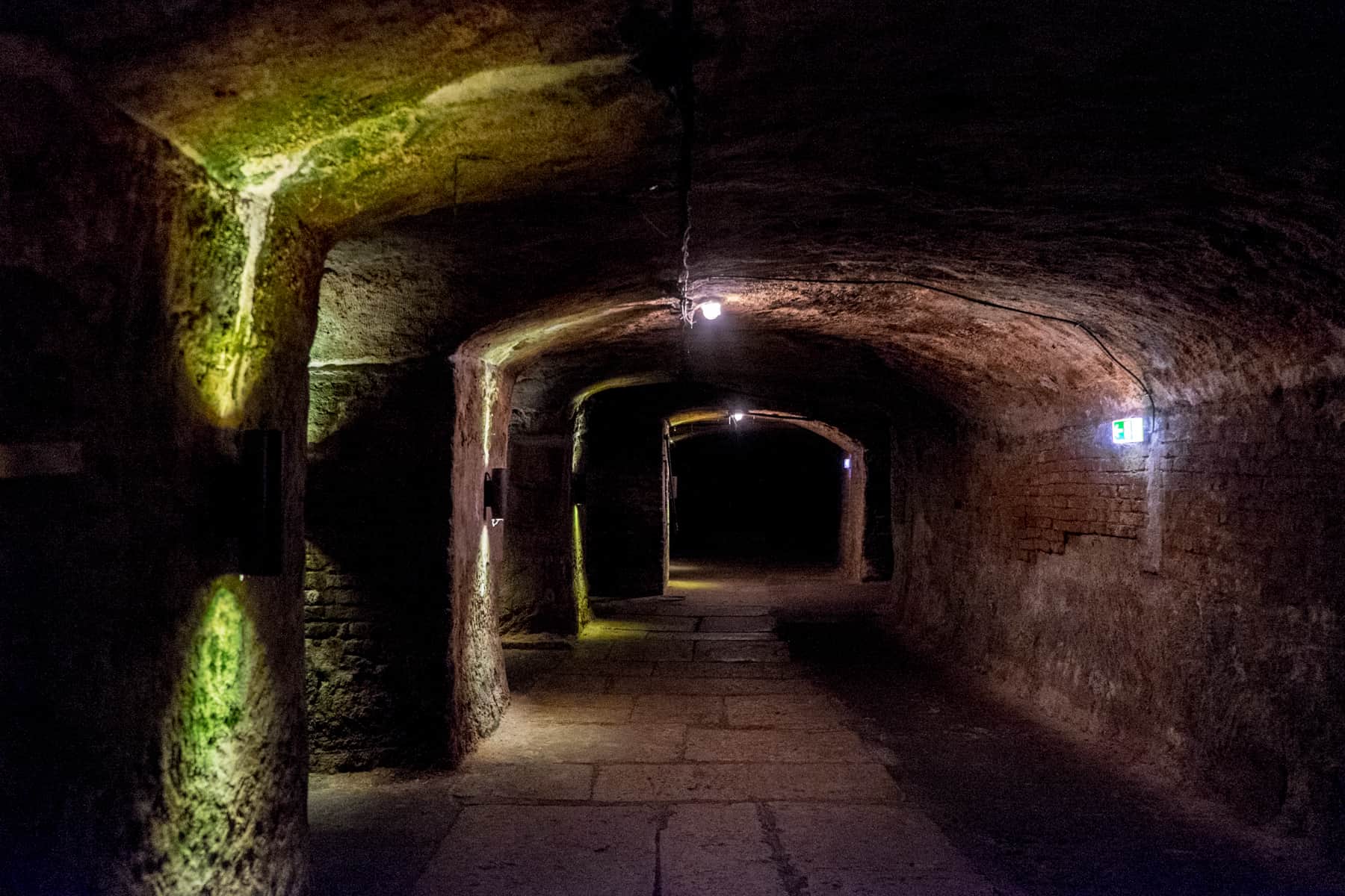 Long dark caverns, lit with yellow, green wall lights mark a pathway inside the historic rock cut beer cellars in Nuremberg