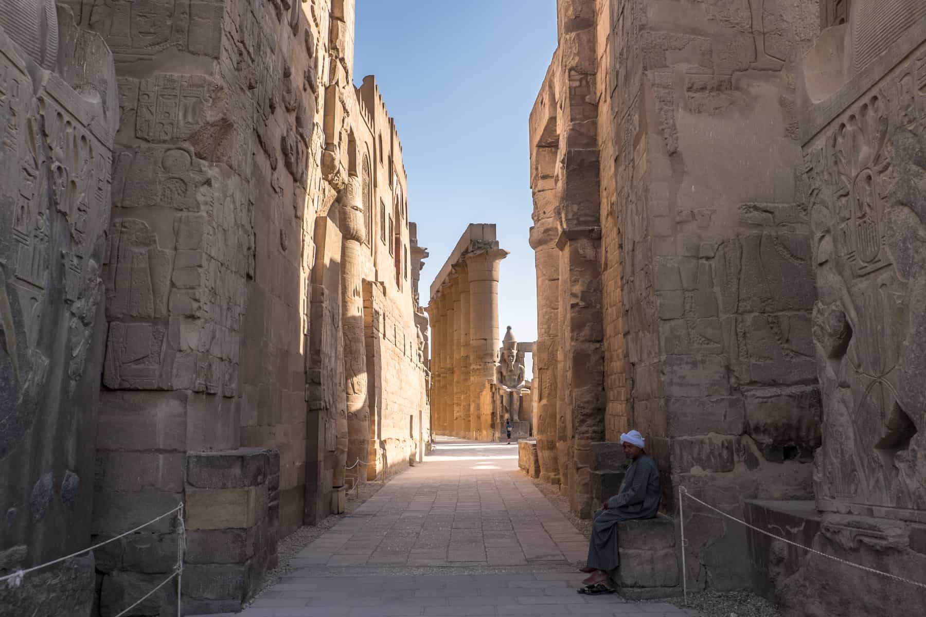An Egyptian temple guard sits within a stone wall corridor filled with sunlight at the Karnak Temple complex - one of the best places to visit in Egypt